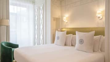 Et pænt møbleret hotelværelse med en stor seng, en grøn lænestol og en lampe på væggen.