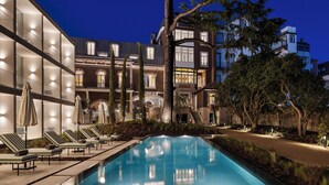 A nighttime pool area with lounge chairs and umbrellas, surrounded by multi-story buildings with illuminated windows. - One Shot Palácio Cedofeita  (Porto)