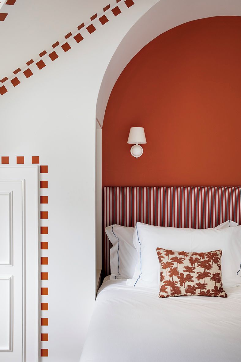 A bedroom with a white door, a red accent wall, a striped headboard, and a single white lamp.