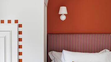 A bedroom with a white door, a red accent wall, a striped headboard, and a single white lamp.