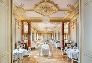 A grand dining hall with ornate ceiling decorations, chandeliers, and a long table set for a meal. - One Shot Palácio Cedofeita  (Porto)