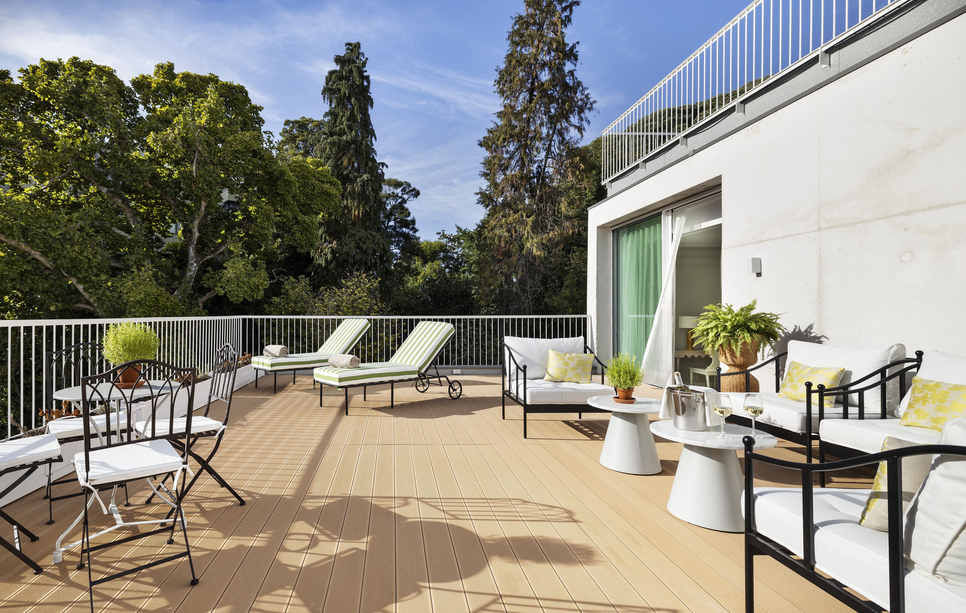A sunlit outdoor deck with lounge chairs, a dining table, and a potted plant.
