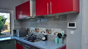 A kitchen with red cabinets, a microwave, a stove, and a coffee maker. - Room-the Blue Room is an Accent of Moder (Antananarivo)
