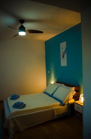 Un lit simple avec une tête de lit, une table de chevet avec une lampe et un ventilateur de plafond.
