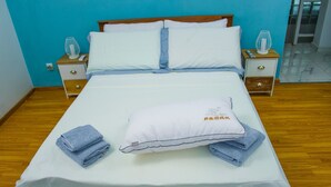 A neatly made bed with white linens and blue towels, a white pillow with text, and wooden nightstands with lamps. - Room-the Blue Room is an Accent of Moder (Antananarivo)