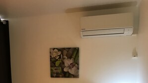 Een hotelkamer met een bed, een nachtkastje met een lamp, een airconditioning en een bloemistisch kunstwerk aan de muur.