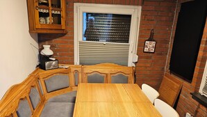 Une pièce chaleureuse avec une table à manger en bois, des bancs rembourrés, une cheminée en briques et une fenêtre avec des stores.