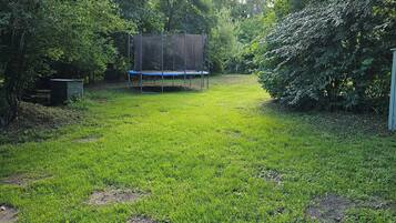 Une cour arrière verdoyante avec un trampoline et un abri de jardin.