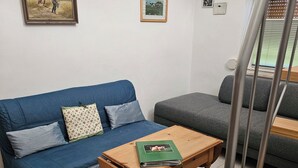 Une pièce avec un canapé bleu, un canapé gris, une table en bois sur laquelle se trouve un dossier vert, et un escalier.