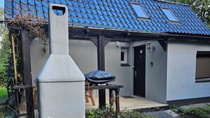 Une maison avec un toit recouvert de tuiles bleues, une cheminée et un petit patio comprenant une table et un barbecue abrité.