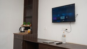 A hotel room with a wooden desk, a coffee maker, a laptop, a remote control, and a water bottle. - Qotel Hotel Rajouri Garden (New Delhi)