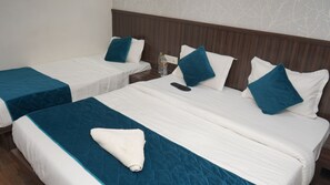 Een hotelkamer met twee enkele bedden, elk met een blauwe sprei en witte kussens. Tussen de bedden staat een nachtkastje met een waterfles en een telefoon.