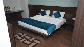 A neatly made bed with a blue blanket and pillows, a wooden headboard, a nightstand with a phone, and a small plant on a shelf.