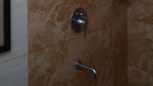 A bathroom with a shower area featuring a handheld showerhead, a wall-mounted faucet, and a control panel. - Qotel Hotel Rajouri Garden (New Delhi)
