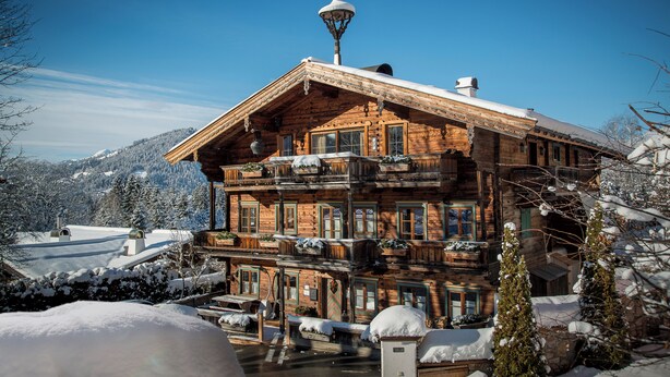 Un chalet de madera de varios pisos con balcones, techo cubierto de nieve y vista a un paisaje montañoso nevado.