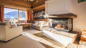 Una sala de estar acogedora con chimenea, paredes de madera y un amplio ventanal con vistas a la montaña.