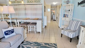 Een woonkamer in strandthema met een bank, een gestreepte fauteuil, een salontafel en een vloerkleed met een schelpenmotief.