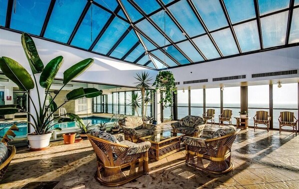 Relax in a spacious indoor area with a high ceiling and glass roof, surrounded by comfortable seating and lush greenery.