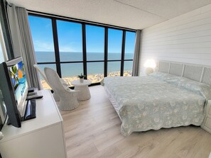 Enjoy a beachside view from the comfort of this room, featuring a bed, bedside table, and wicker chairs.