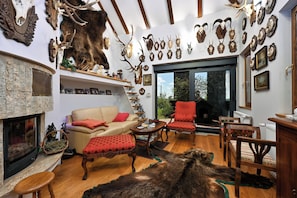 A room with a fireplace, a sofa, red chairs, and a variety of mounted animal skulls on the walls. - Hunting Lodge (Velika Pisanica)