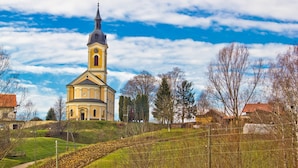 A church with a prominent bell tower, surrounded by a hilly landscape and sparse trees. - Hunting Lodge Hills Retreat (Velika Pisanica)