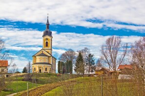A church with a prominent bell tower, surrounded by a hilly landscape and sparse trees. - Hunting Lodge Hills Retreat (Velika Pisanica)