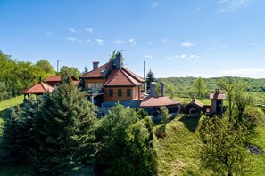 A large house with multiple sections, surrounded by dense greenery and hills in the background.