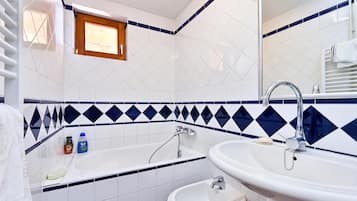 A bathroom with a bathtub, a sink, and a bidet. There is a window above the bathtub and a towel rack to the right.