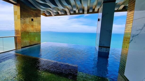 A infinity pool with a clear view of the ocean and distant land. - Pattaya Seaview Beachfront Skypool Copacabana Jomtien Condo (Pattaya City)