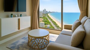 A modern living room with a large window offering a view of a beach and cityscape. - Pattaya Seaview Beachfront Skypool Copacabana Jomtien Condo (Pattaya City)