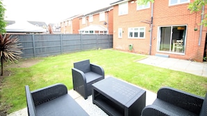 A backyard with a patio area, including wicker furniture and a brick building in the background.