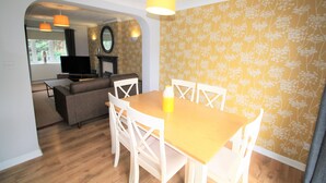 A dining area with a wooden table and white chairs, a yellow pendant light, and a floral wallpaper pattern.