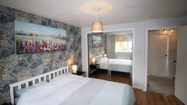 A bedroom with a large bed, a nightstand, a lamp, and a painting on the wall.