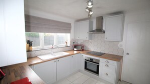 A kitchen with white cabinets, a microwave, an oven, a sink, and a window with a view of the outside.