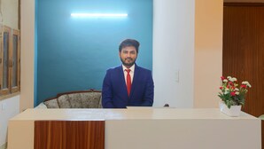 A reception desk with a blue wall and a wooden panel. - Hotel Glinzer Palace By Aura (Noida)