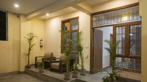 A reception area with a wooden desk, chairs, and potted plants. - Hotel Glinzer Palace By Aura (Noida)