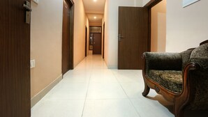 A hallway with wooden doors, a plush armchair, and a tiled floor. - Hotel Glinzer Palace By Aura (Noida)