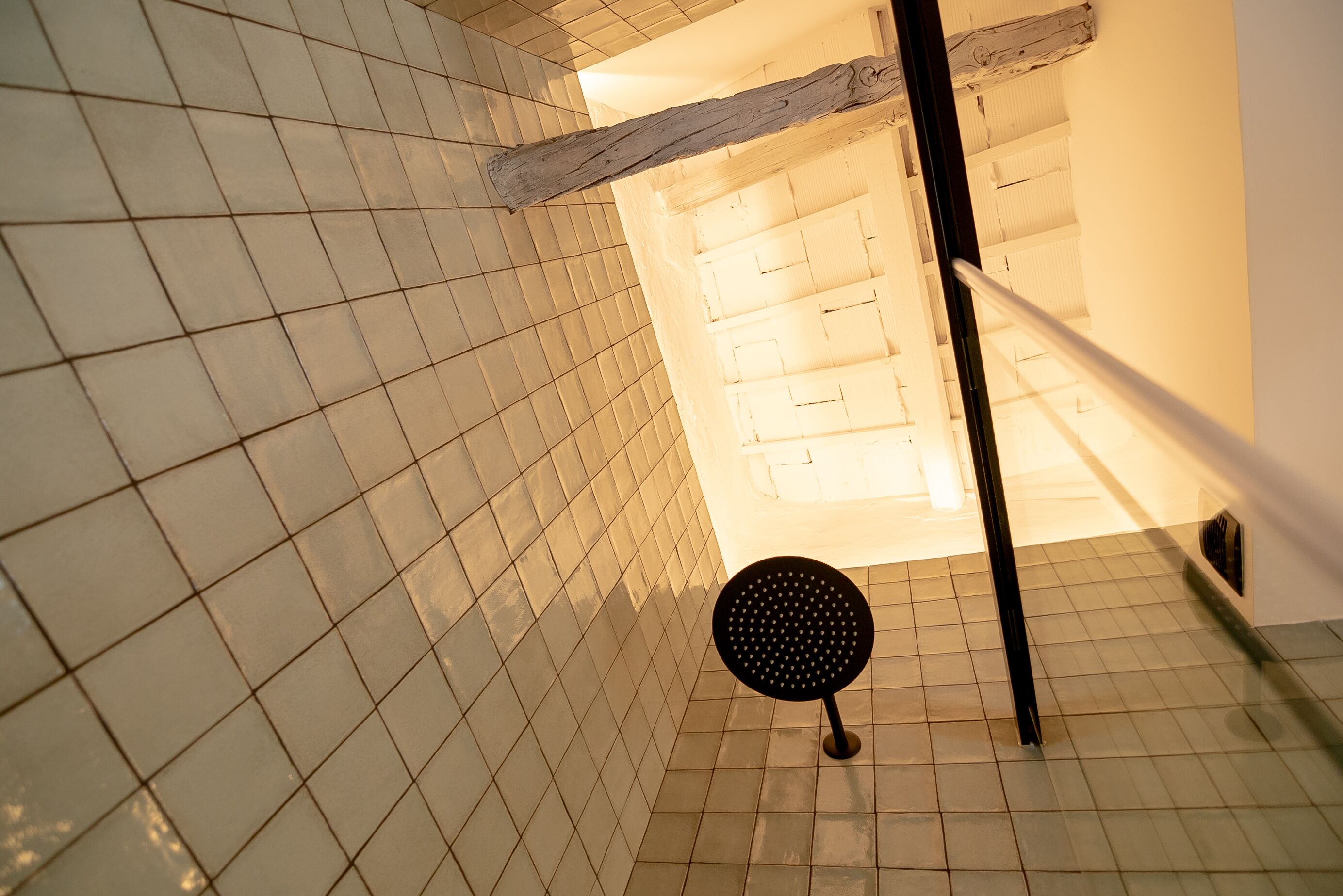 Un baño con baldosas, una viga de madera y un objeto circular negro en el suelo.