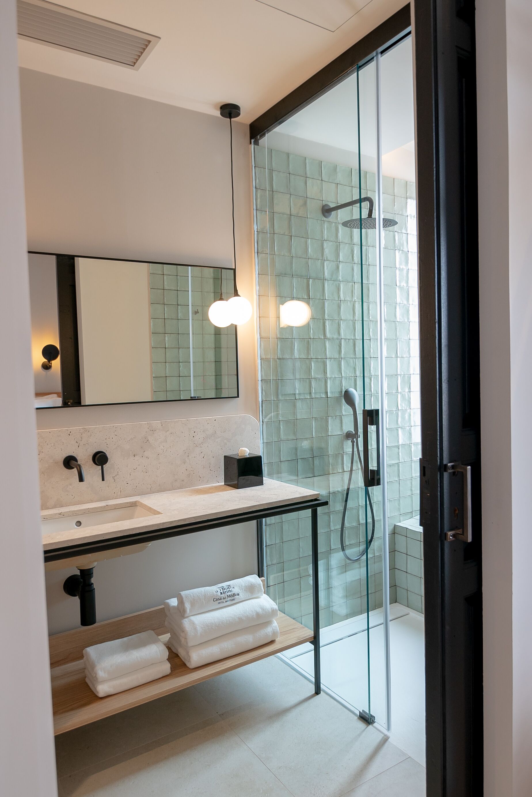 Un baño moderno con cabina de ducha de vidrio, lavamanos de mármol y repisa de madera con toallas.