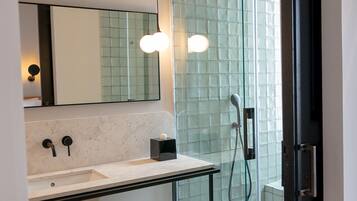 Un baño moderno con cabina de ducha de vidrio, lavamanos de mármol y repisa de madera con toallas.