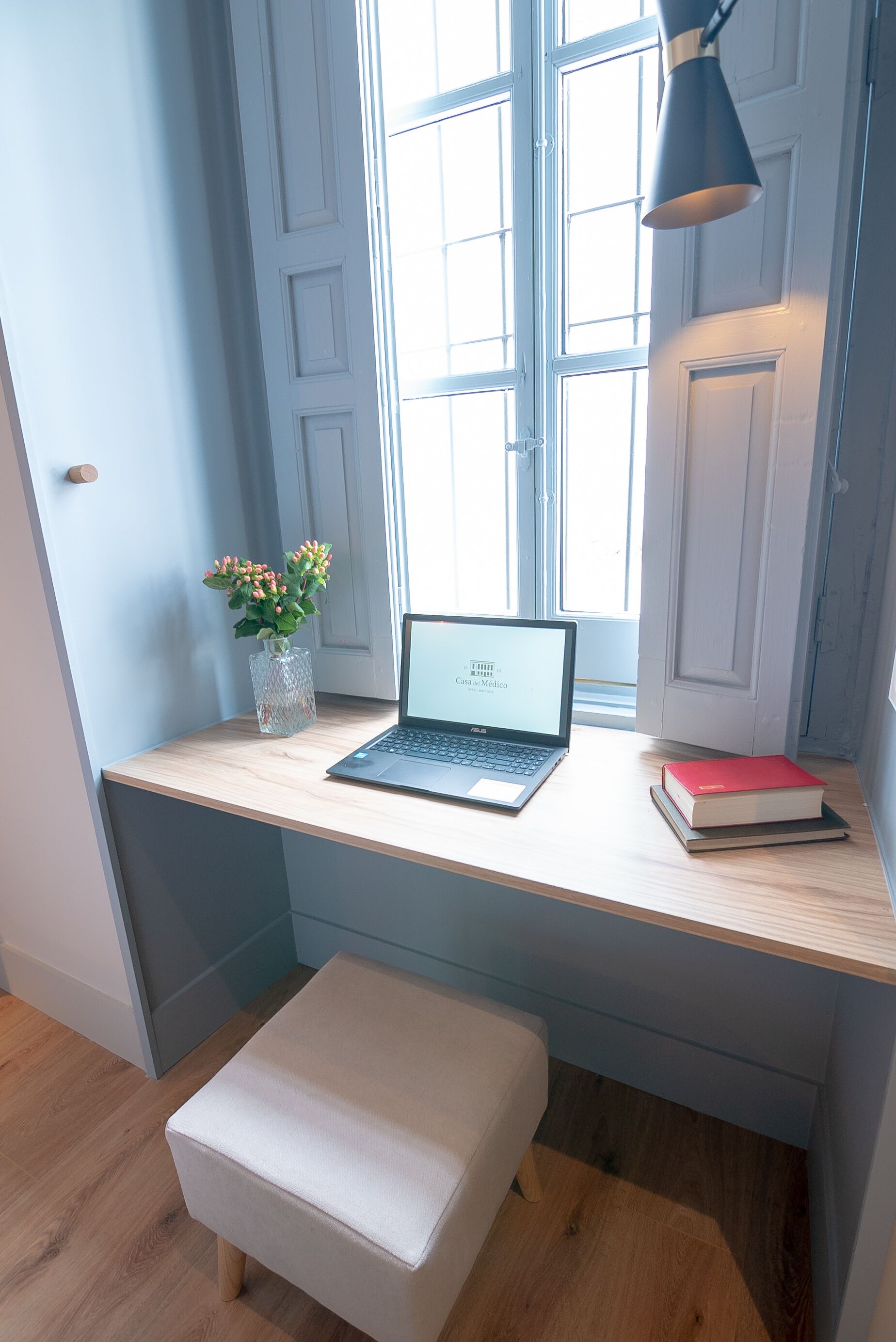 Un petit espace de travail comprenant un ordinateur portable, un vase avec des fleurs et un livre posés sur un bureau en bois.