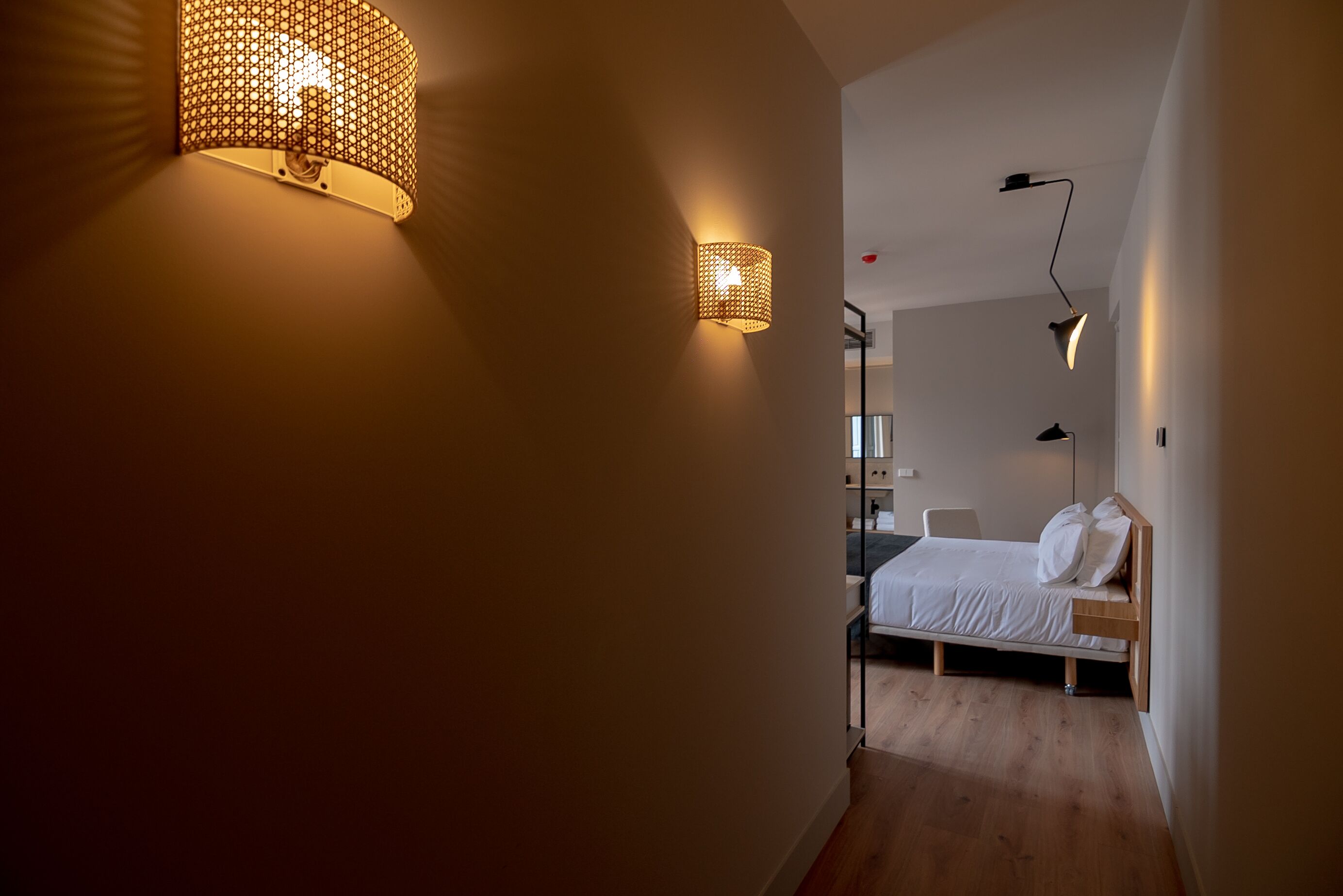 A narrow hallway with a bed in the background, a wall-mounted light fixture, and a hanging light.