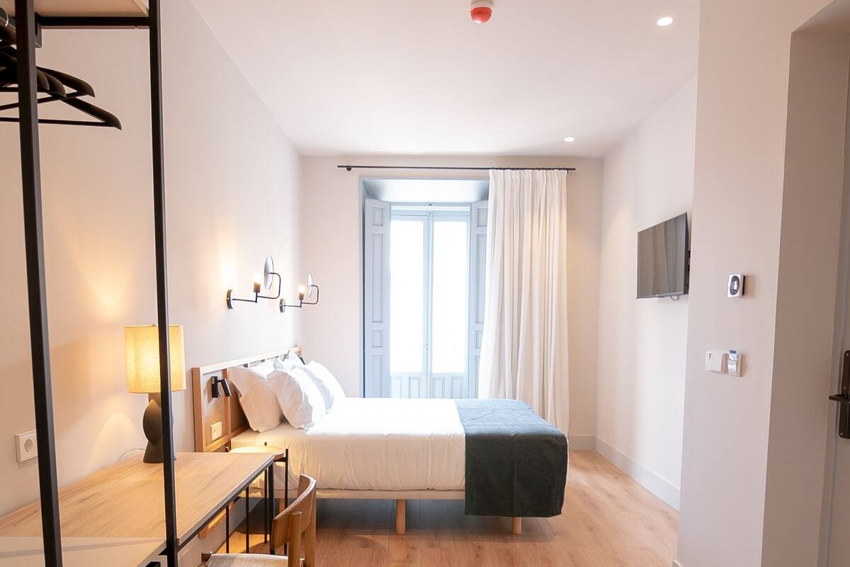 A modern bedroom with a bed, desk, chair, and a television on the wall.