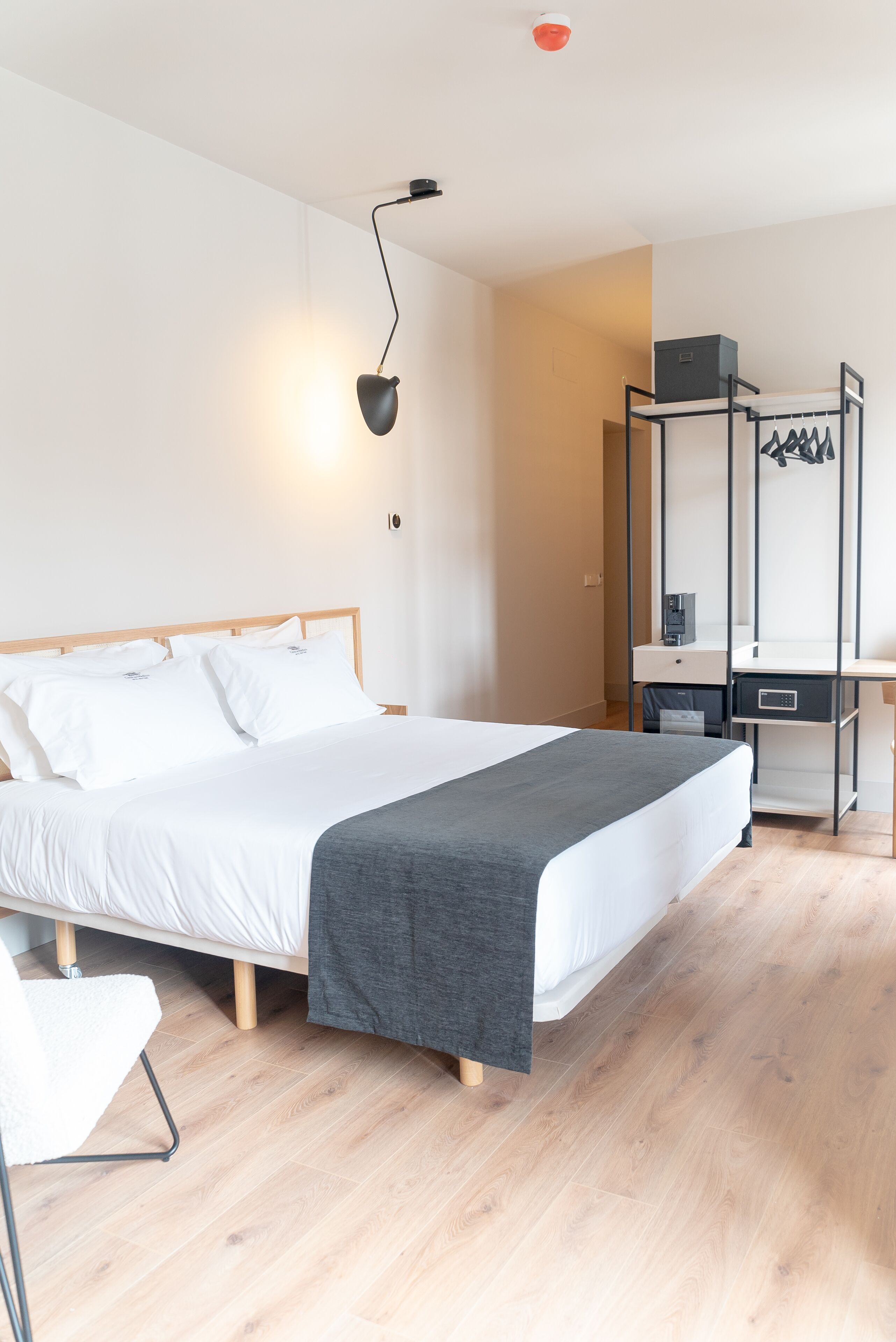 A modern hotel room with a large bed, a desk, a chair, and a wardrobe.