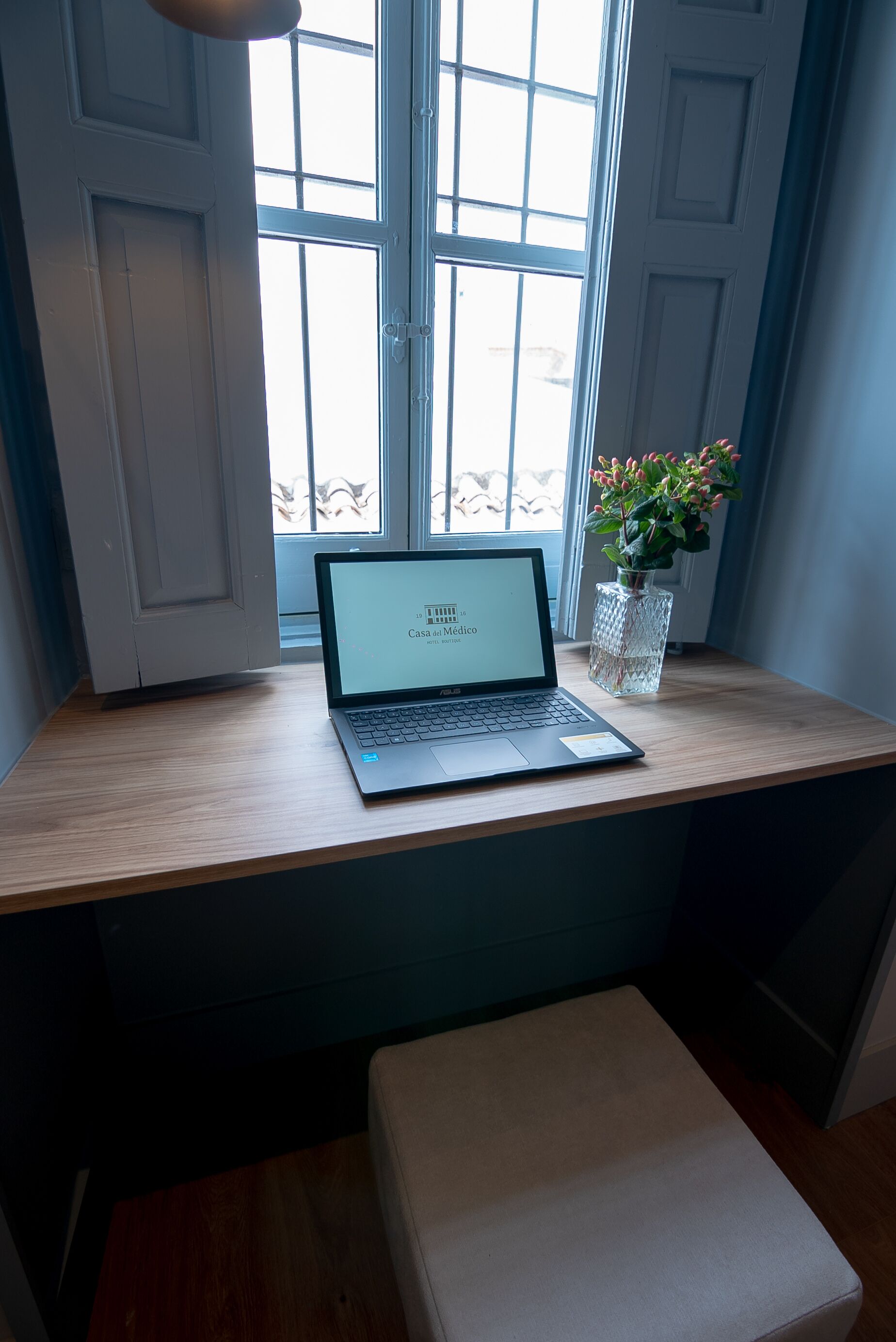 A laptop on a wooden desk near a window with a view of the outside.