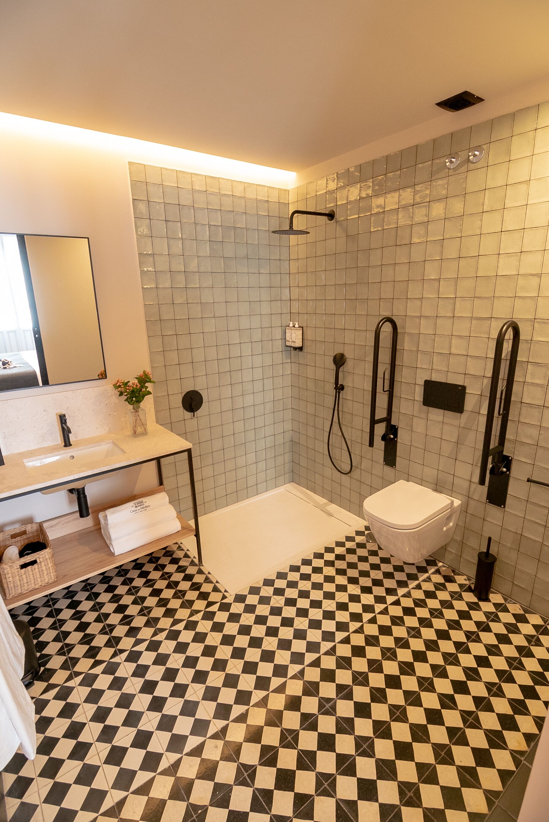 A modern bathroom with a checkered floor, a glass shower enclosure, a white sink, and a toilet.