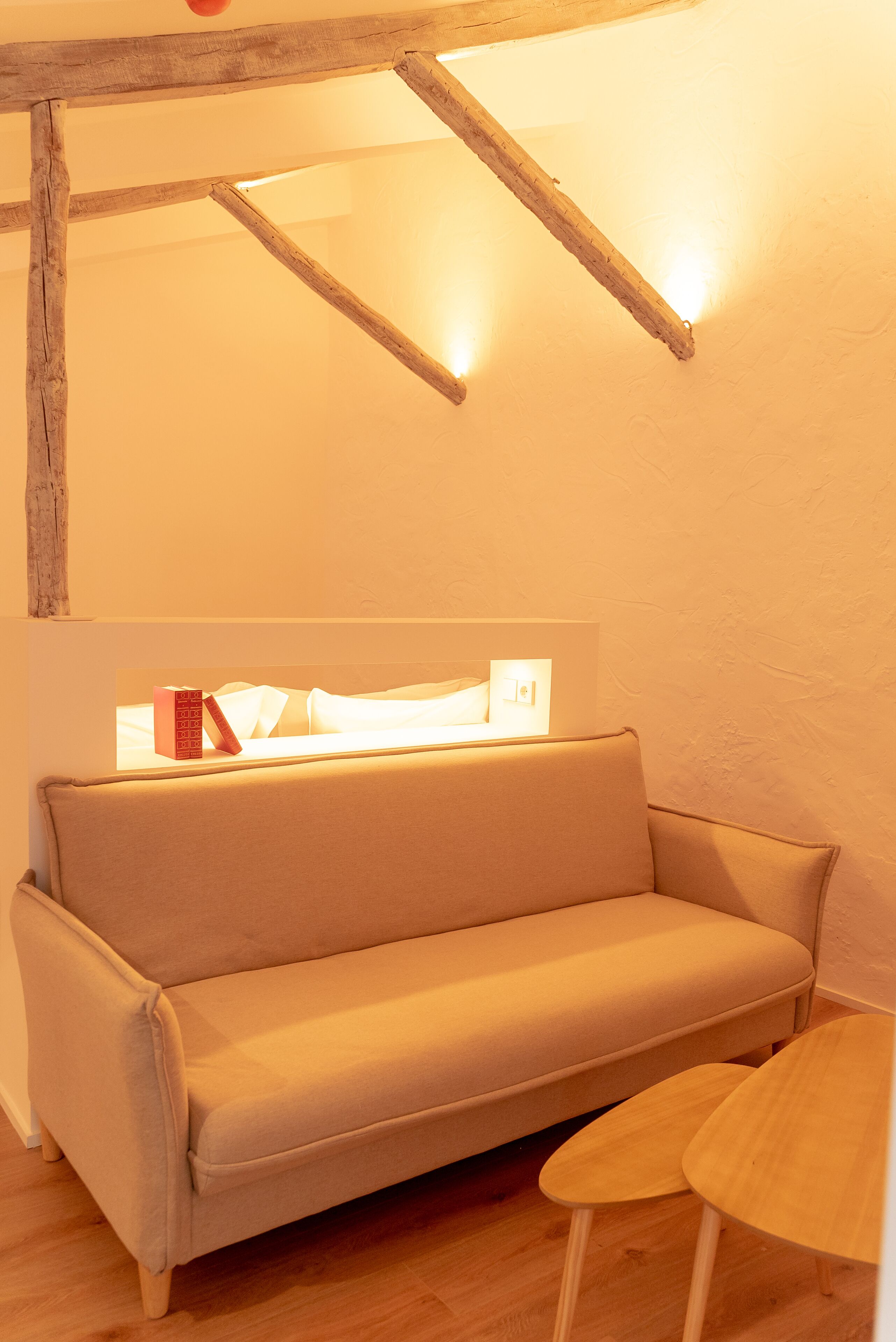 A cozy room with a beige sofa, a small wooden table, and a slanted ceiling with exposed beams.