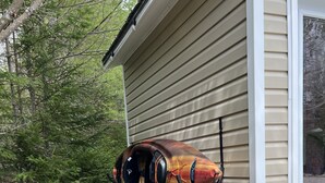 Deux kayaks appuyés contre une maison, avec un chemin de gravier et des arbres à proximité.