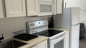 Une cuisine moderne avec des meubles blancs, un évier en acier inoxydable, une plaque de cuisson noire et un réfrigérateur blanc.