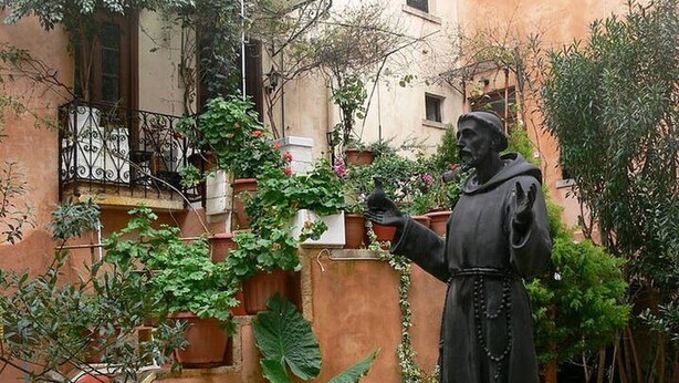 Una estatua en un patio rodeado de plantas en macetas y un edificio con balcones.